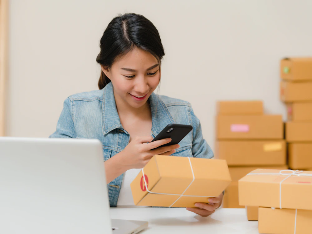 Entrepreneur checking an order on her phone next to boxes ready to ship